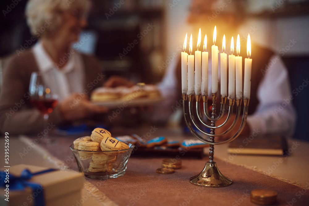 Traditional Hanukkah candles in menorah with senior couple in background.