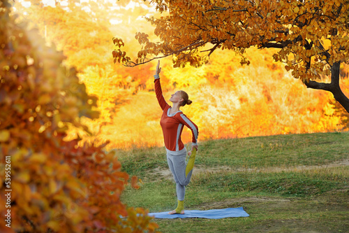 Woman practicing one leg yoga pose under the autumn tree
