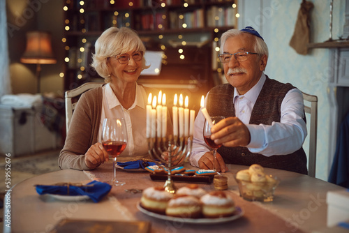Fotografía Happy senior couple lighting candles in menorah while celebrating Hanukkah at home