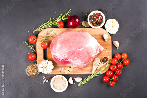 Top view on boneless raw pork shoulder ready for roasting with seasonings and vegetables over dark concrete background. Organic meat for main dish. View above photo