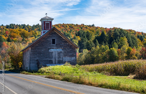 Small wooden barn with red cupola set against vibrant Vermont fall colors