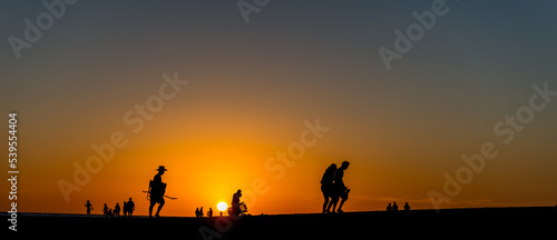 Panoramic view of silhouettes of a group of people walking along the coastline at a beautiful sunset photo
