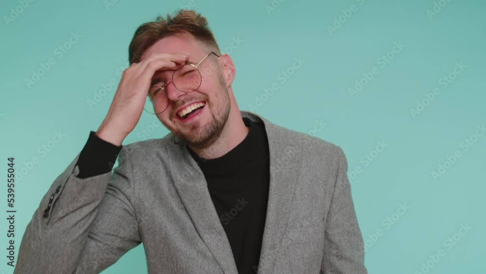 Amused happy business man in jacket pointing finger to camera, laughing out loud, taunting making fun of ridiculous appearance, funny joke. Young guy boy posing alone on blue studio wall background Amused happy business man in jacket pointing finger to camera, laughing out loud, taunting making fun of ridiculous appearance, funny joke. Young guy boy posing alone on blue studio wall background