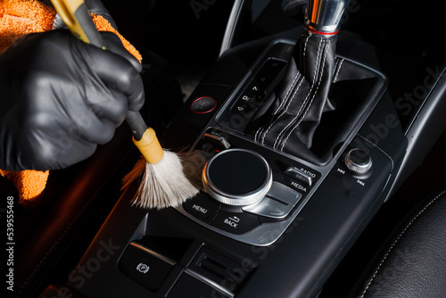 Dry cleaning with brush of gearbox and dashboard in car. Auto detailing service. Cleaning individual elements of black leather interior in auto.