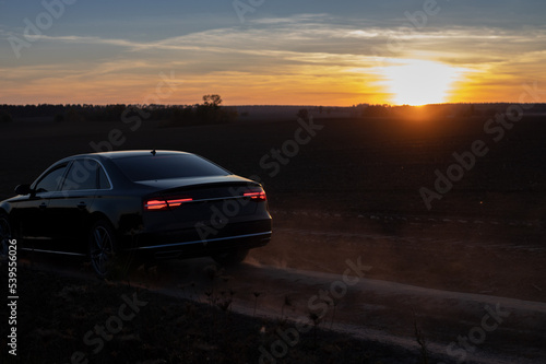 car drives along a country road in the evening against the backdrop of a beautiful orange sunset. Backlight  outlines of the car. freedom of movement  vacation  adventure  road trip