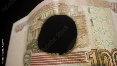 The camera passes through a hole in a Russian banknote, one hundred rubles. Money is burning, smoke. Dolly slider, extreme close-up.