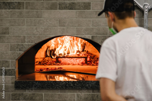 The chef puts the Margherita, four cheese or meat pizza on a shovel in the oven. A firewood oven for cooking and baking pizza. Italian traditional pizza is cooked in a stone wood-fired oven. Back view