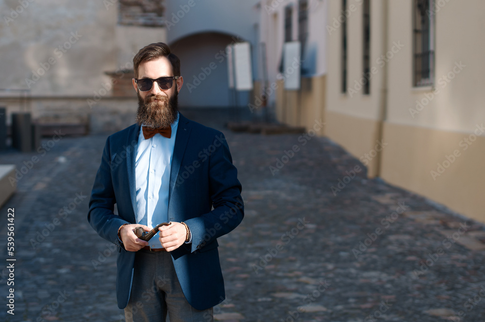 Stylish man with beard wearing a jacket, shirt and bow tie with a pipe