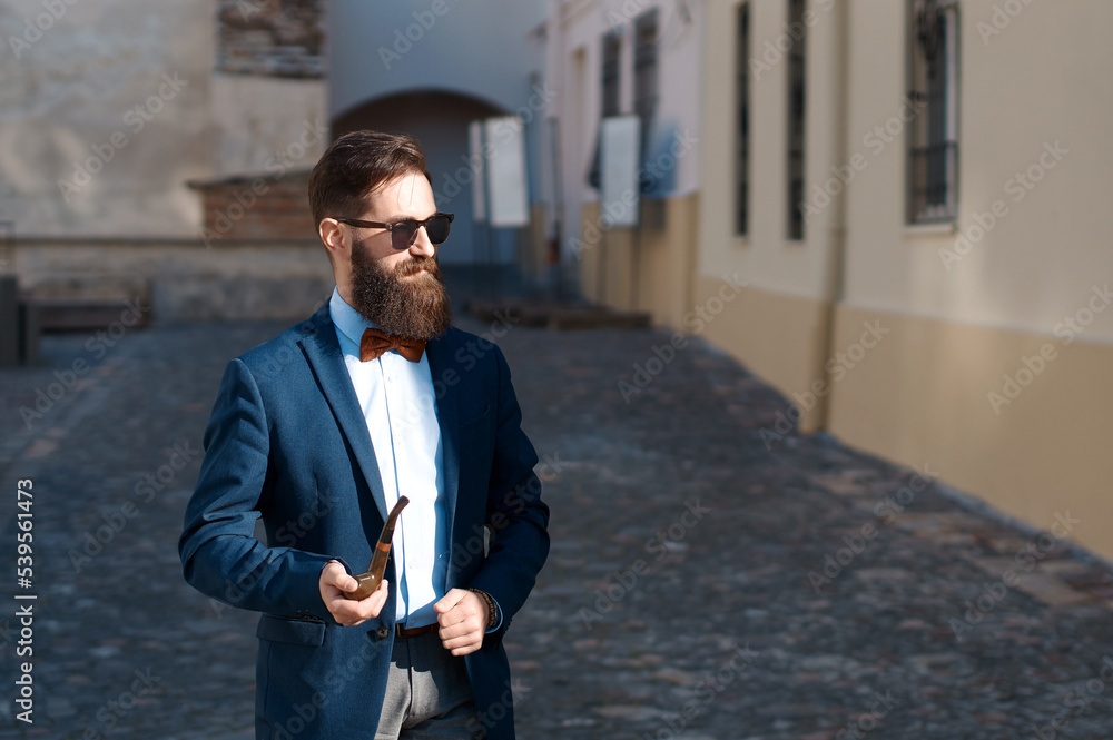 Stylish man with beard wearing a jacket, shirt and bow tie with a pipe
