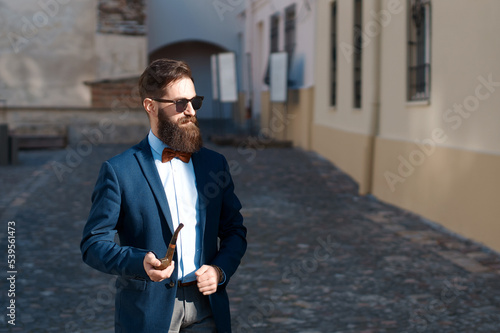 Obraz na płótnie Stylish man with beard wearing a jacket, shirt and bow tie with a pipe w salonie