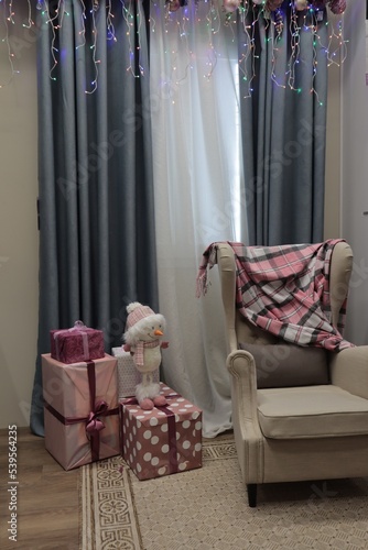 Decorated room with Christmas decorations, gifts, a snowman and a chair with a blanket.