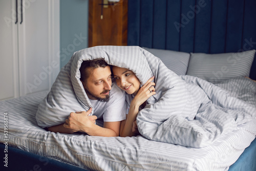 couple in love in white clothes lying under a blanket on the bed in the bedroom in the morning.