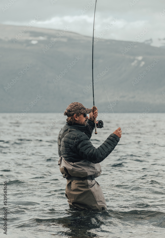 Fisherman immersed in the water of a lake with a fly rod Fisherman immersed in the water of a lake with a fly rod