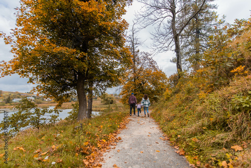 Fototapeta Naklejka Na Ścianę i Meble -  Beautiful autumn lanscapes. Father, mother, and child are walking along a path covered with leaves. It's autumn time.