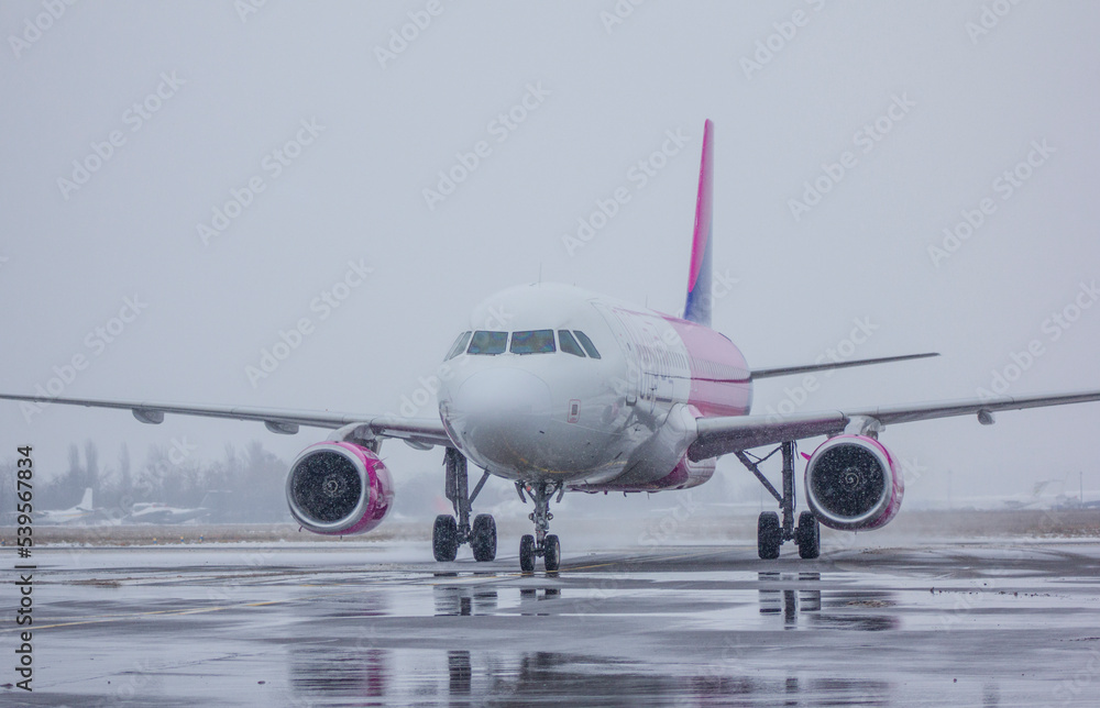 Obraz premium A jet passenger airliner moves along an airport taxiway in winter, against a cloudy sky