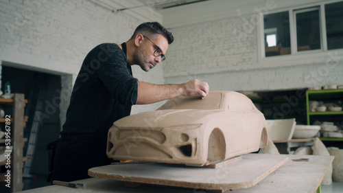 Valokuva A ceramist works closely on the design details of an unfinished eco friendly electric car prototype sculpture made of raw clay