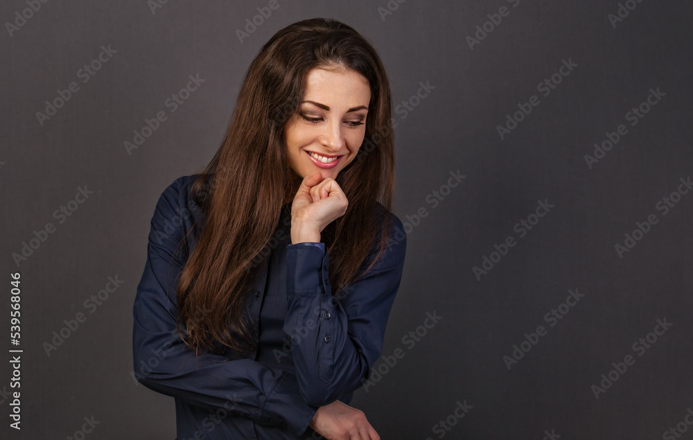 Beautiful confident thinking smiling business woman with folded arms, long brown hair in blue shirt on grey background looking down with empty copy space for text. Closeup Beautiful confident thinking smiling business woman with folded arms, long brown hair in blue shirt on grey background looking down with empty copy space for text. Closeup