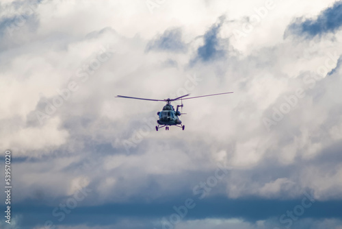 A military helicopter flies against the background of an overcast sky and against the background of heapy clouds, front view 