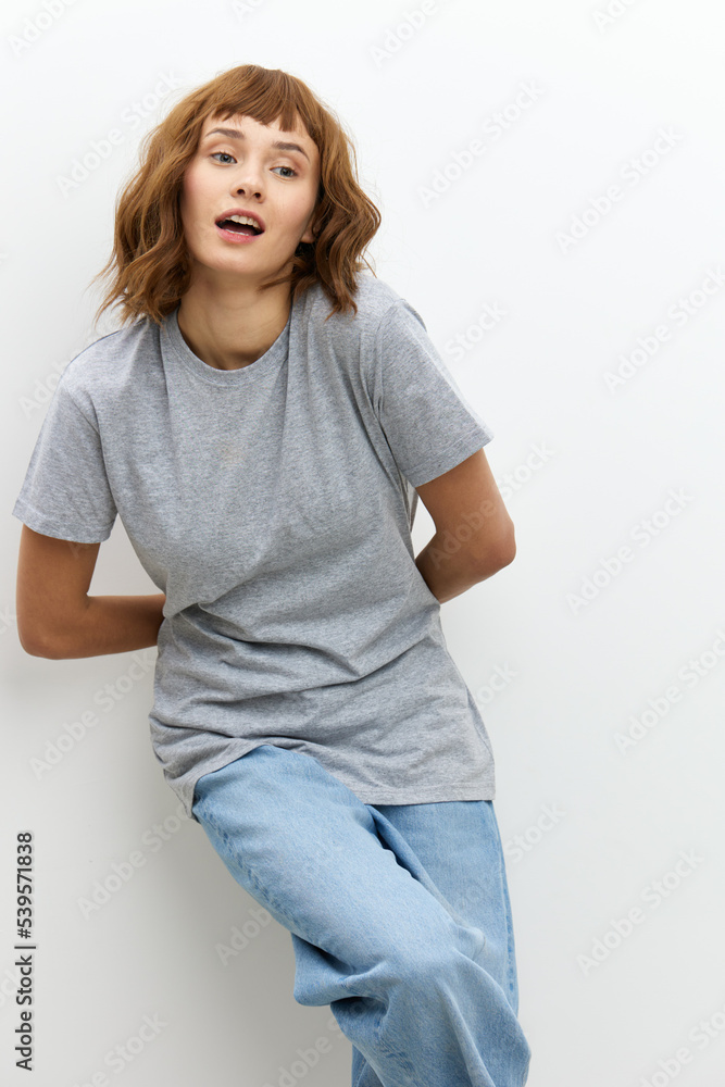 a wide-smiling, joyful woman stands in a gray T-shirt on a white background, leaning against the wall. Vertical Studio Photography a wide-smiling, joyful woman stands in a gray T-shirt on a white background, leaning against the wall. Vertical Studio Photography