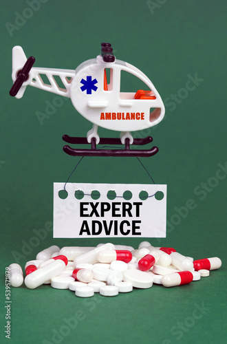 On a green surface, an ambulance helicopter, pills and a white sign with the inscription - EXPERT ADVICE
