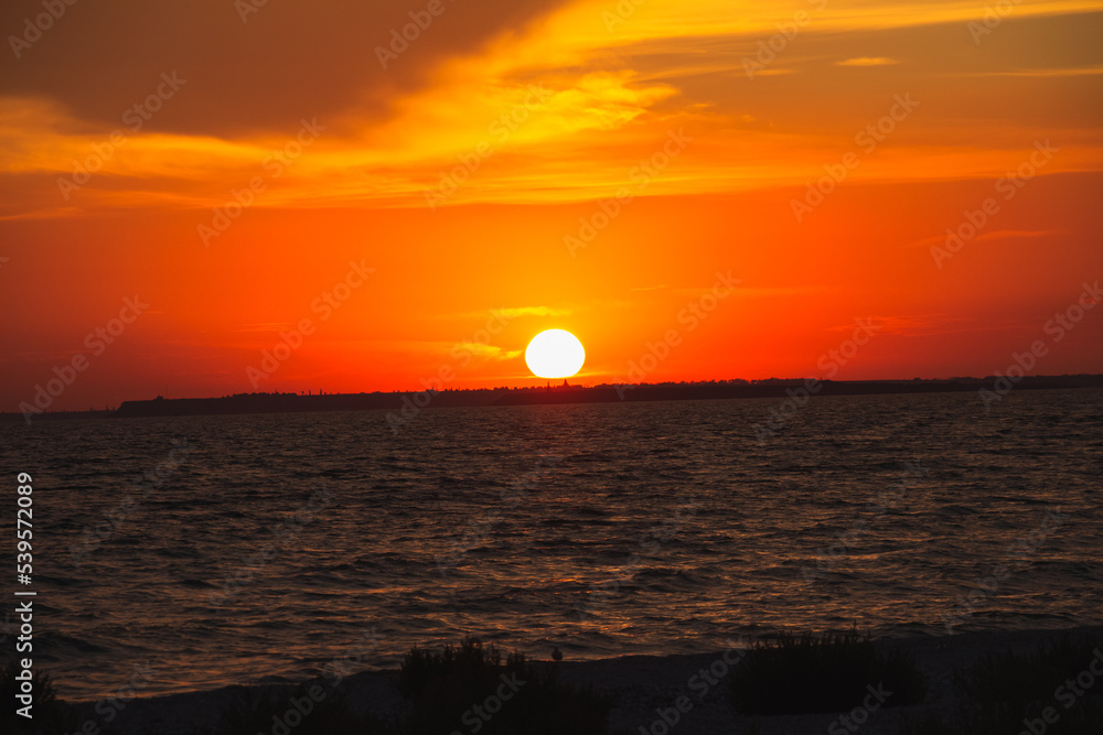 Amazing Black sea. Clouds and sand landscape background. Drama orange sky and red sun on horizon. Golden blue hour at the ocean romantic evening. Tropical island summer paradise. Wild rest in camp.