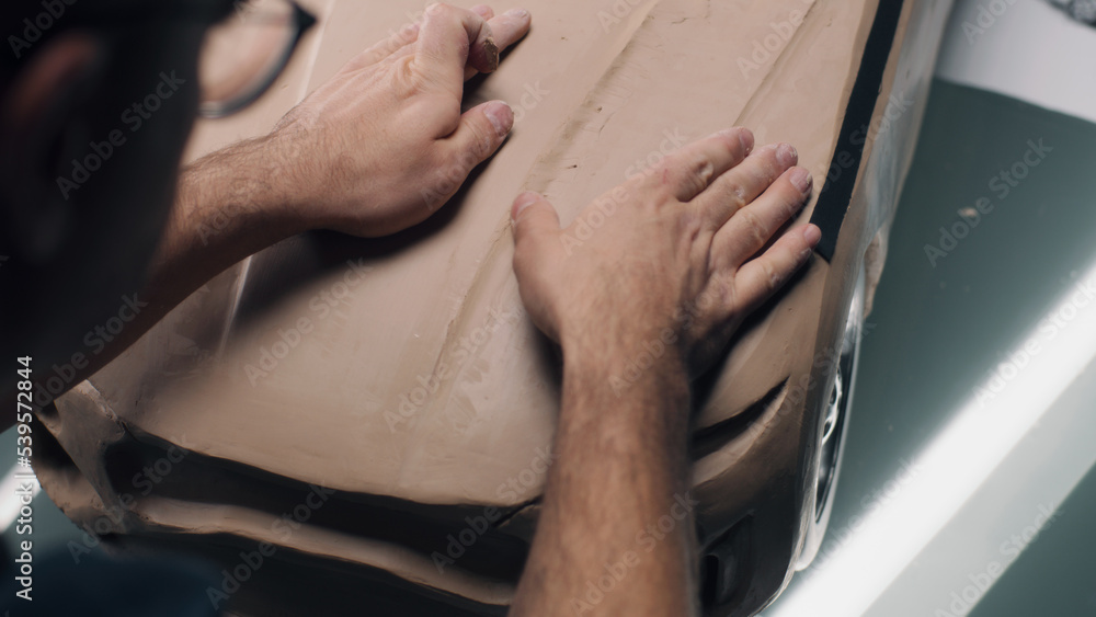 High angle shot of male automotive designer sculpting futuristic car model from plasticine clay. Future design of new generation electric car. Working in modern car design studio.