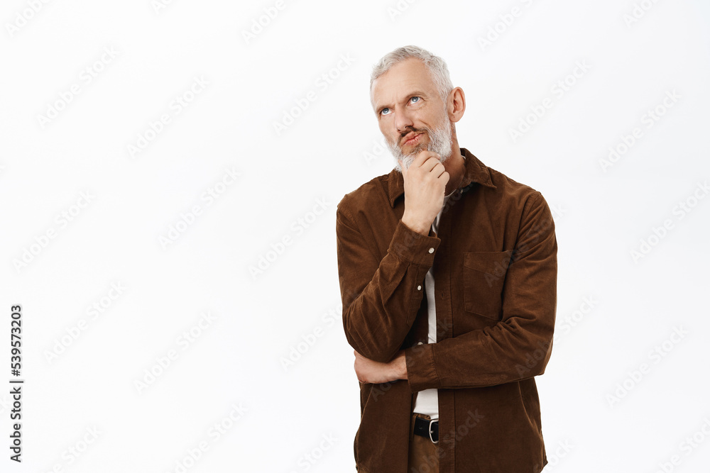 Thoughtful mature man, senior guy touching beard and thinking, pondering smth, standing against white background
