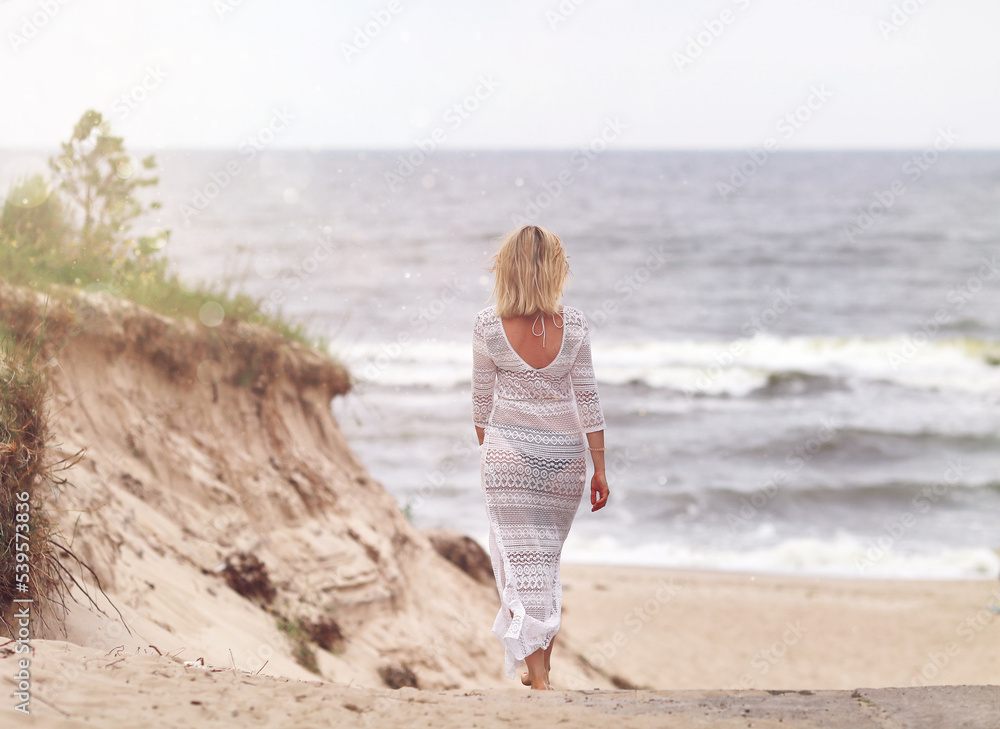 Woman in white dress walking on the beach in the morning