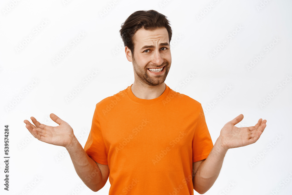 Man with confused face, shrugs shoulders, shows empty hands and makes guily smile, stands over white background Man with confused face, shrugs shoulders, shows empty hands and makes guily smile, stands over white background