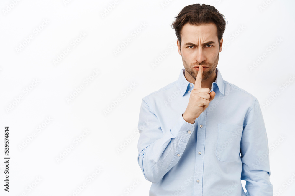 Angry man shushing, press finger to lips and hush, tell to be quiet, standing over white background Angry man shushing, press finger to lips and hush, tell to be quiet, standing over white background