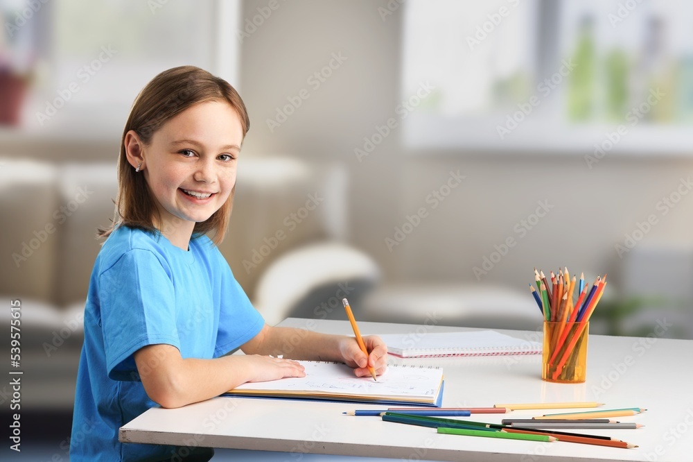 Happy schoolgirl sitting at desk, classroom background Happy schoolgirl sitting at desk, classroom background