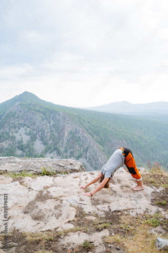 Deep deflection of the back of the asana dog muzzle down, man doing yoga in the mountains, Adho mukha shvanasana, guy training in nature, stretching the body, flexible back