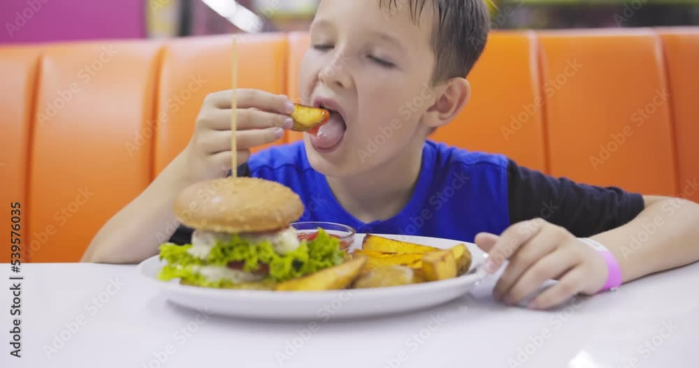 Child eating hamburger and French fries in a fast food restaurant Child eating hamburger and French fries in a fast food restaurant
