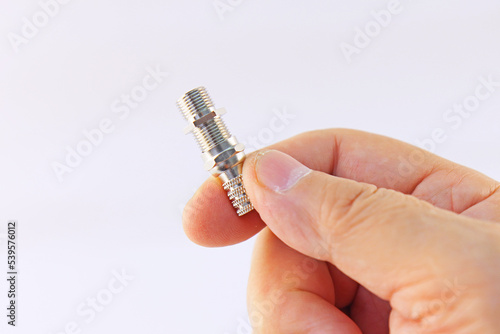 A hand holds a connector for connecting a coaxial cable on a white background.
