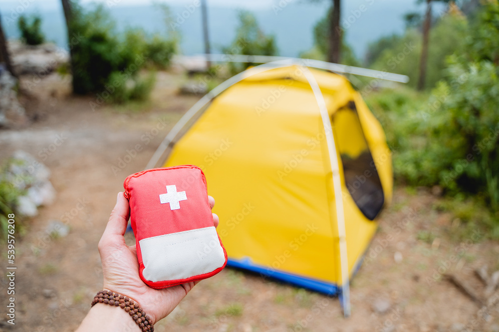 First aid kit in the mountains, extreme set of medicines, red first aid kit on the background of the tent, equipment on a hike, hand holding a minibag with medicines