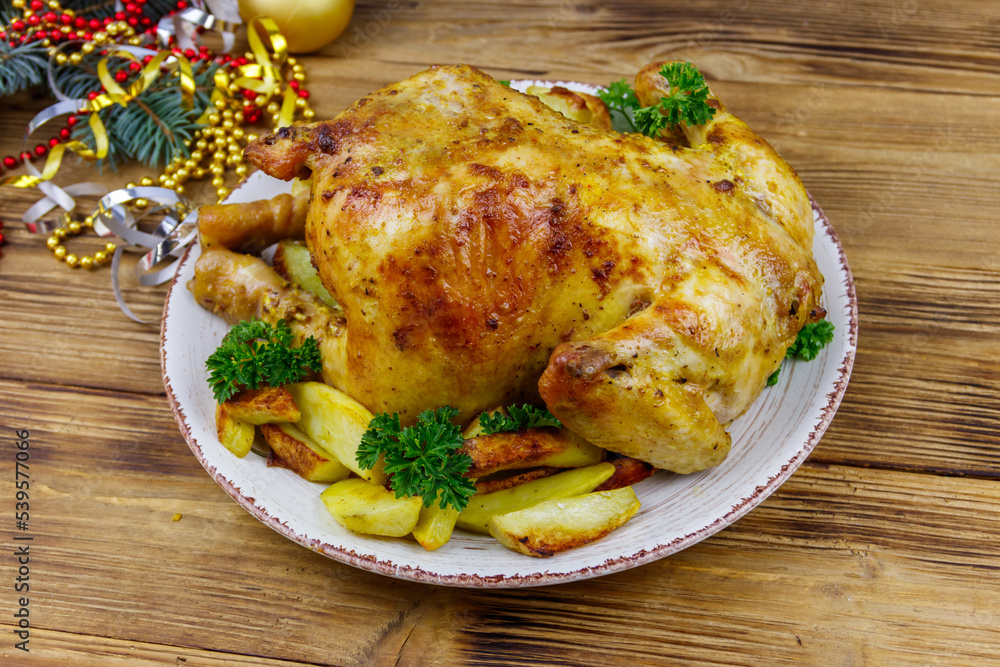 Baked whole chicken with potato and Christmas decorations on a wooden table Baked whole chicken with potato and Christmas decorations on a wooden table