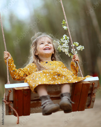 beautiful little girl on a swing with a cherry blossom branch in her hands