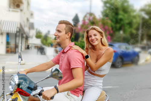 Happy couple in love riding a motorbike on summer city streets ,man and woman travel . Young riders enjoying themselves on trip. Adventure and vacations concept.