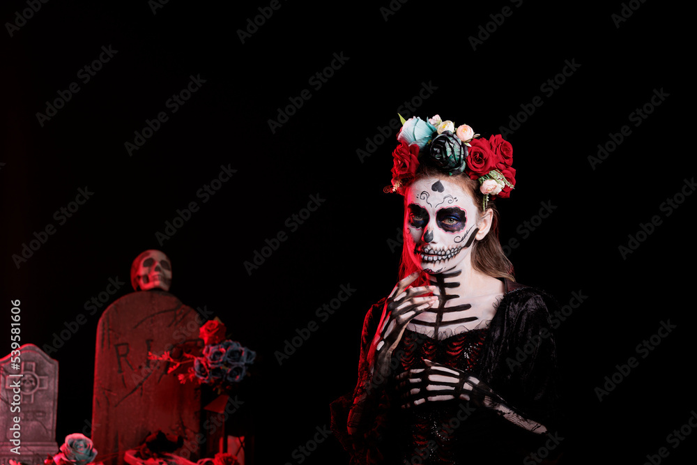 Beautiful young woman with sugar skull make up and crown of roses, dressed in black costume of death as santa muerte. Day of the dead halloween art to celebrate holy mexican tradition.