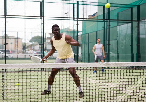Portrait of sporty man playing with male partner padel doubles game on outdoors court