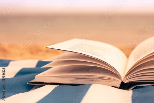 A opened book sitting on the beach sand with a ocean background. Literature and reading.