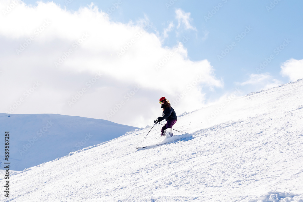 Women in winter overalls skiing on fresh powder snow hill at mountains at winter alpine ski resort