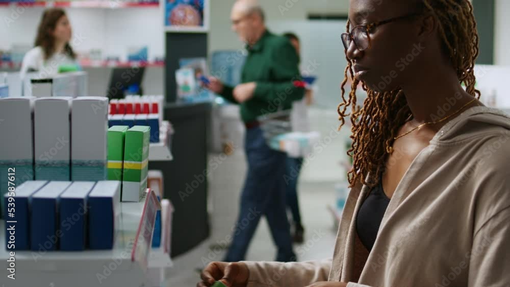 Female client looking at boxes of medicaments to cure disease, having prescription treatment and checking supplements packages on shelves. Buying medicaments and pills from pharmacy shop. Female client looking at boxes of medicaments to cure disease, having prescription treatment and checking supplements packages on shelves. Buying medicaments and pills from pharmacy shop.