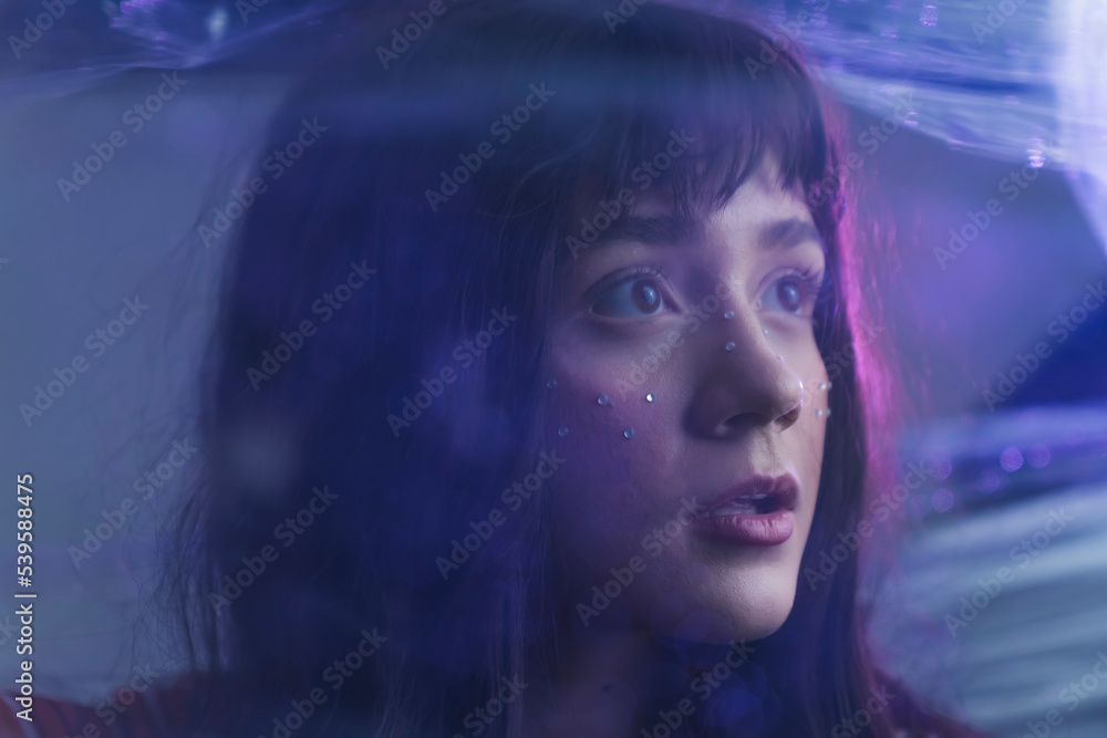 White teenage girl with purple hair looking away from camera with anxious expression behind layer of plastic wrap. Artistic portrait. Horizontal shot. High quality photo White teenage girl with purple hair looking away from camera with anxious expression behind layer of plastic wrap. Artistic portrait. Horizontal shot. High quality photo