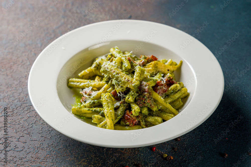 Pasta with sun-dried tomatoes and pesto on dark stone table