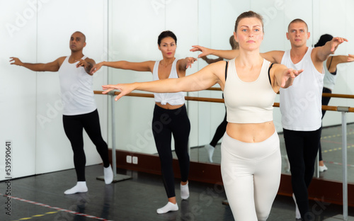 Concentrated women and men rehearsing ballet dance in studio.