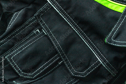 White stitching on black fabric. Texture of black working clothes white stitching closeup, green reflective elements © Karamelity