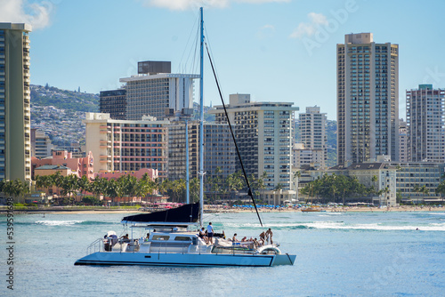 Catamaran sailboat navigating in front of Waikiki beach in Honolulu, Hawaii - Tourists on a sightseeing cruise off O'ahu island in the Pacific Ocean