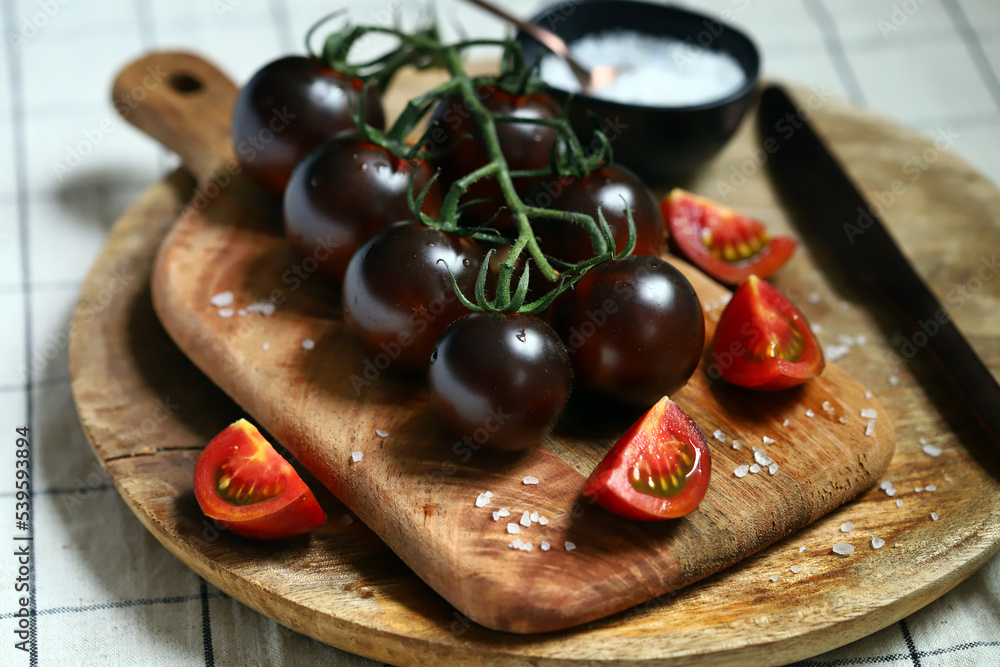 Black tomatoes on a branch on a wooden board with sea salt.