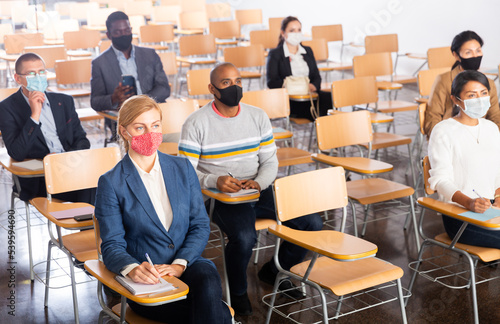 Group of diverse business people wearing face masks for viral protection and keeping social distance listening to speaker at conference, the new normal